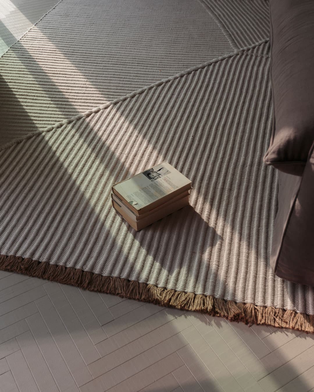 A striped rug with fringed edges on a light floor, under a sofa. A closed book with a photo on the cover rests on the rug.