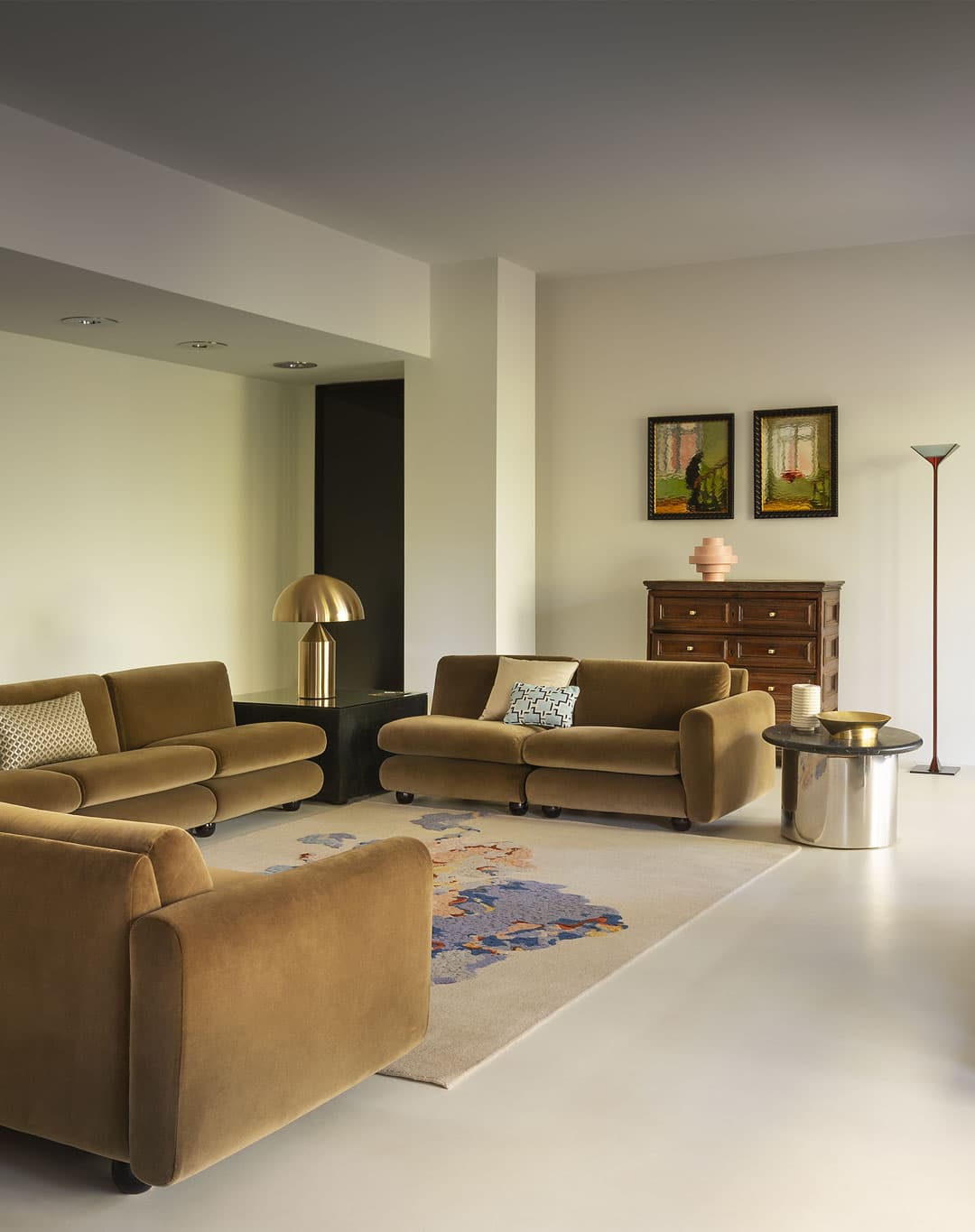 Modern living room with cozy sofas, a patterned rug, a brass lamp, a wooden chest of drawers, and a tall floor lamp.