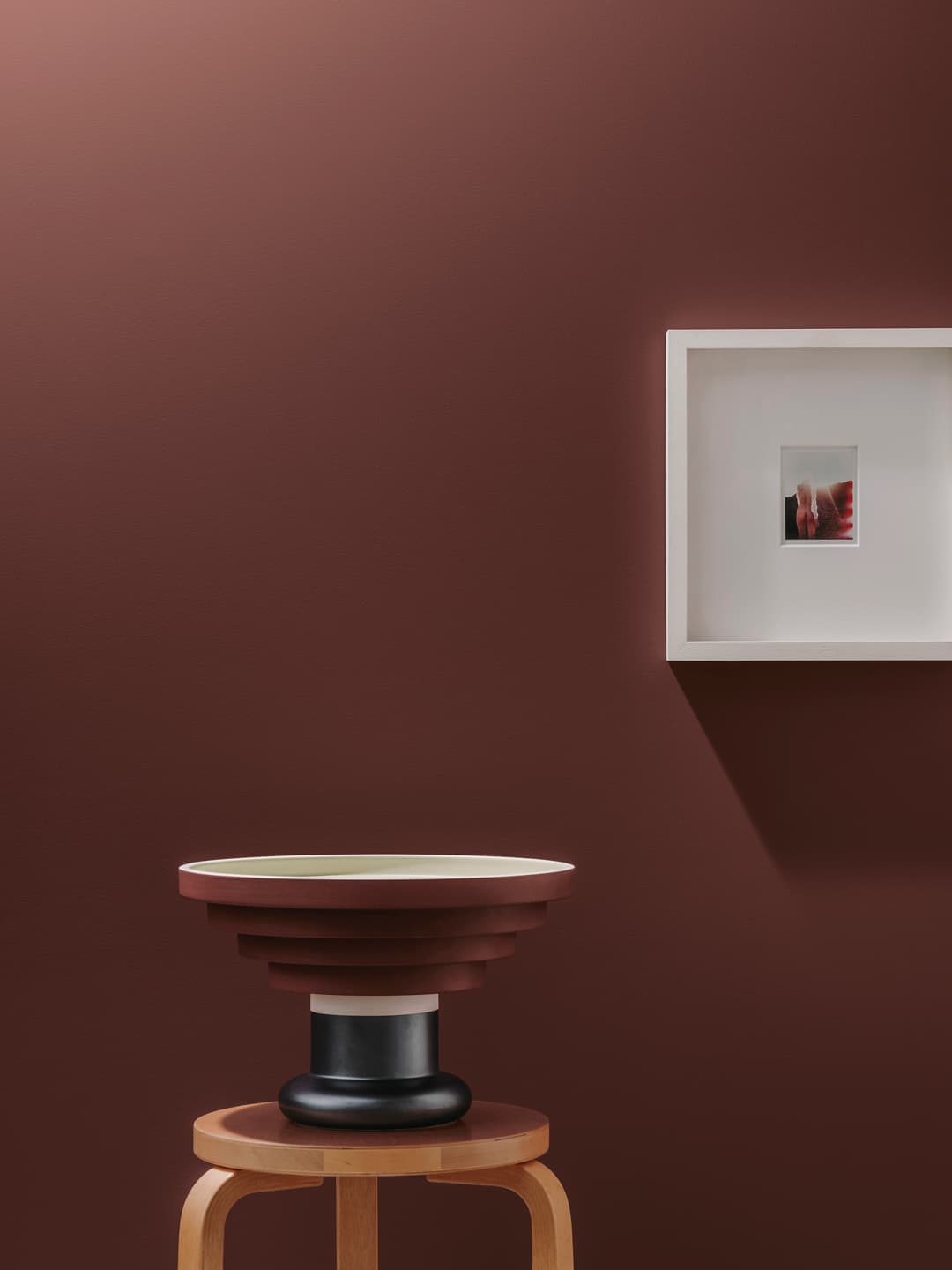 A wooden stool, set against a bordeaux wall.