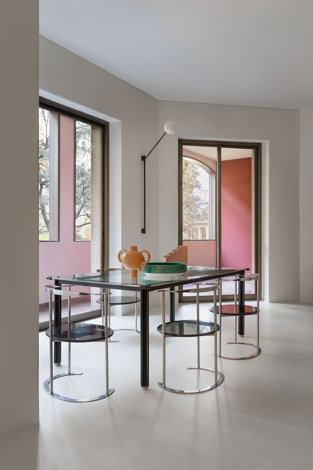 Modern dining room with a glass table, four metal chairs, and a decorative vase.