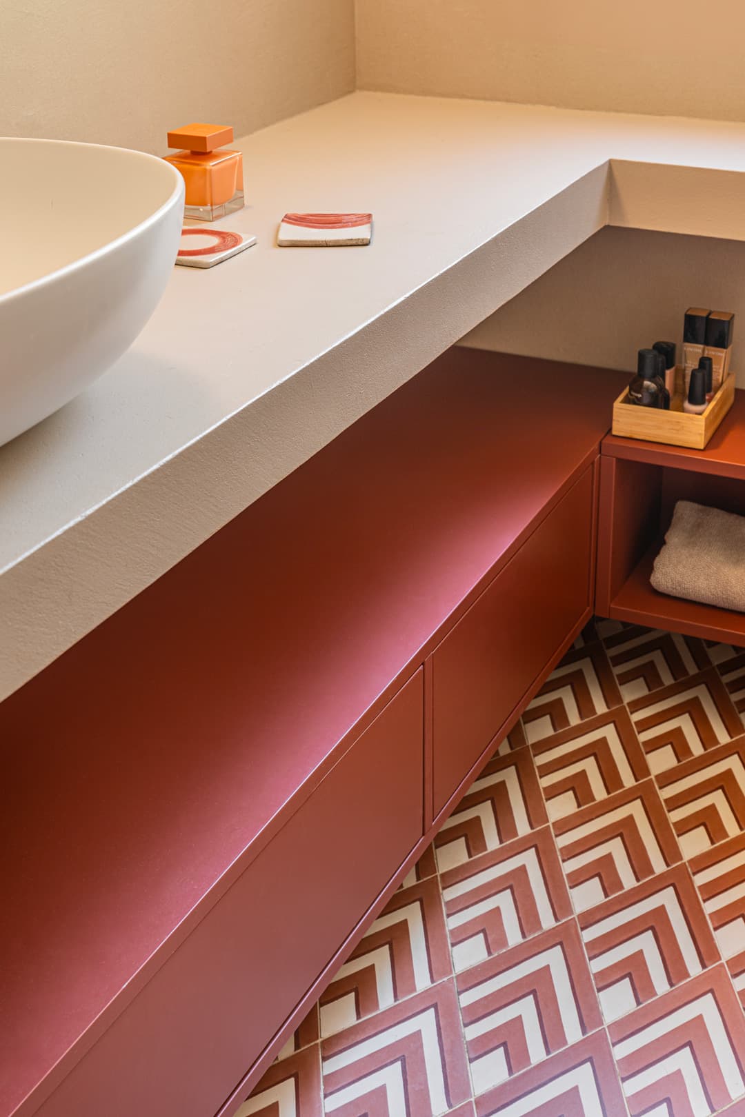 Bathroom with geometric patterned floor tiles, a white countertop with a vessel sink, and red cabinets. Toiletries are neatly arranged.