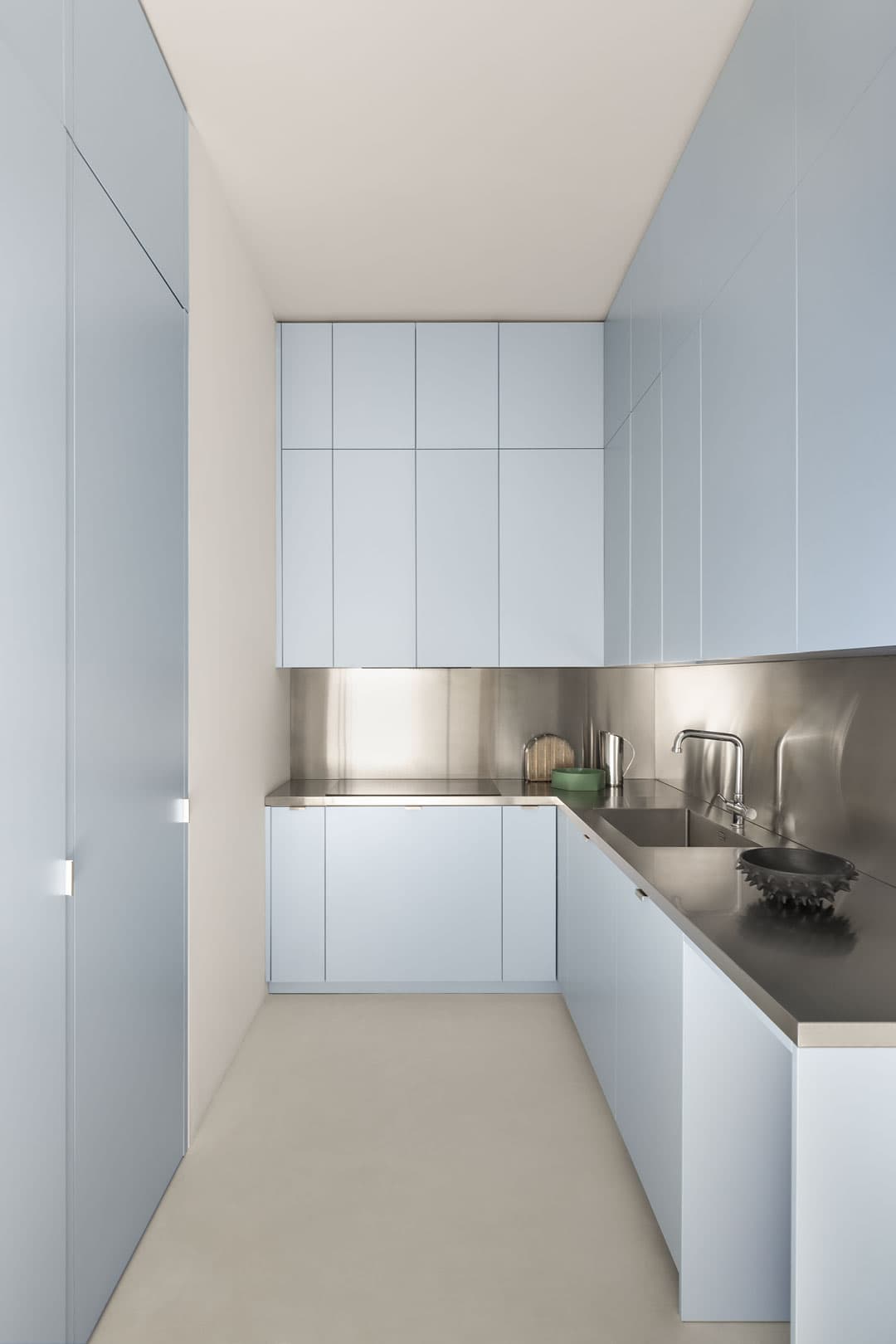 Minimalist kitchen with light blue cabinets, stainless steel countertops, and backsplash. Neutral walls and floor enhance the sleek design.