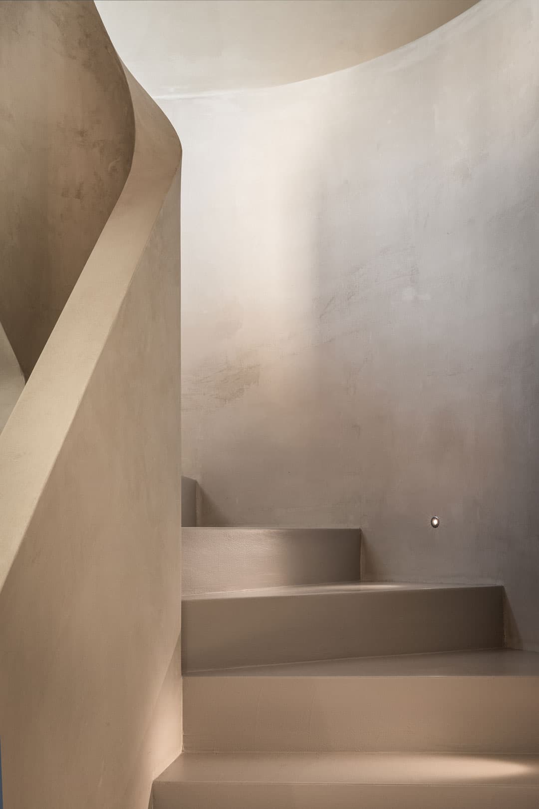 Minimalist spiral staircase, light beige walls and steps, creating a serene and modern architectural look.