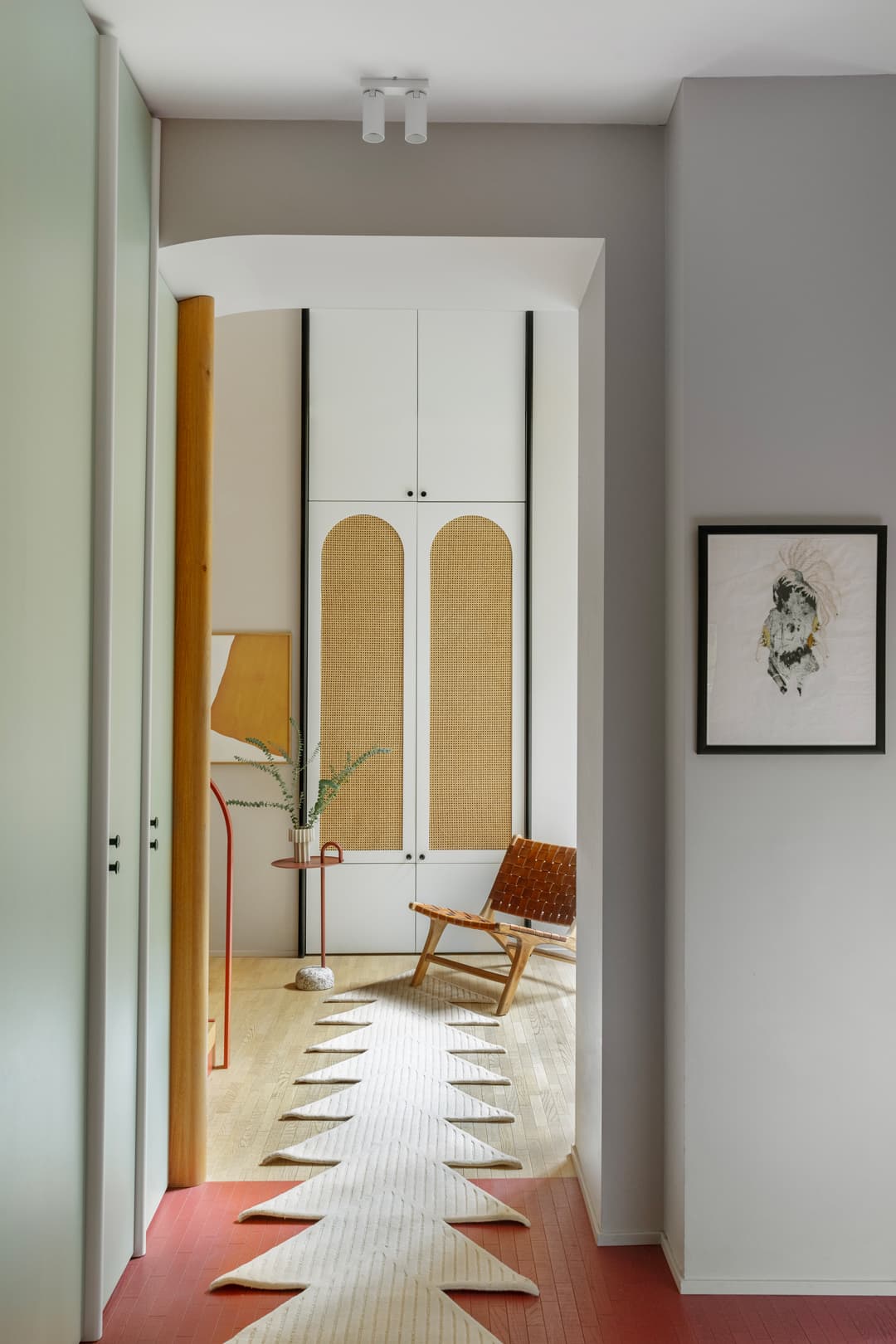 A modern hallway with a geometric rug, wicker chair, and artwork on the wall. Light wood flooring and neutral tones create a cozy ambiance.