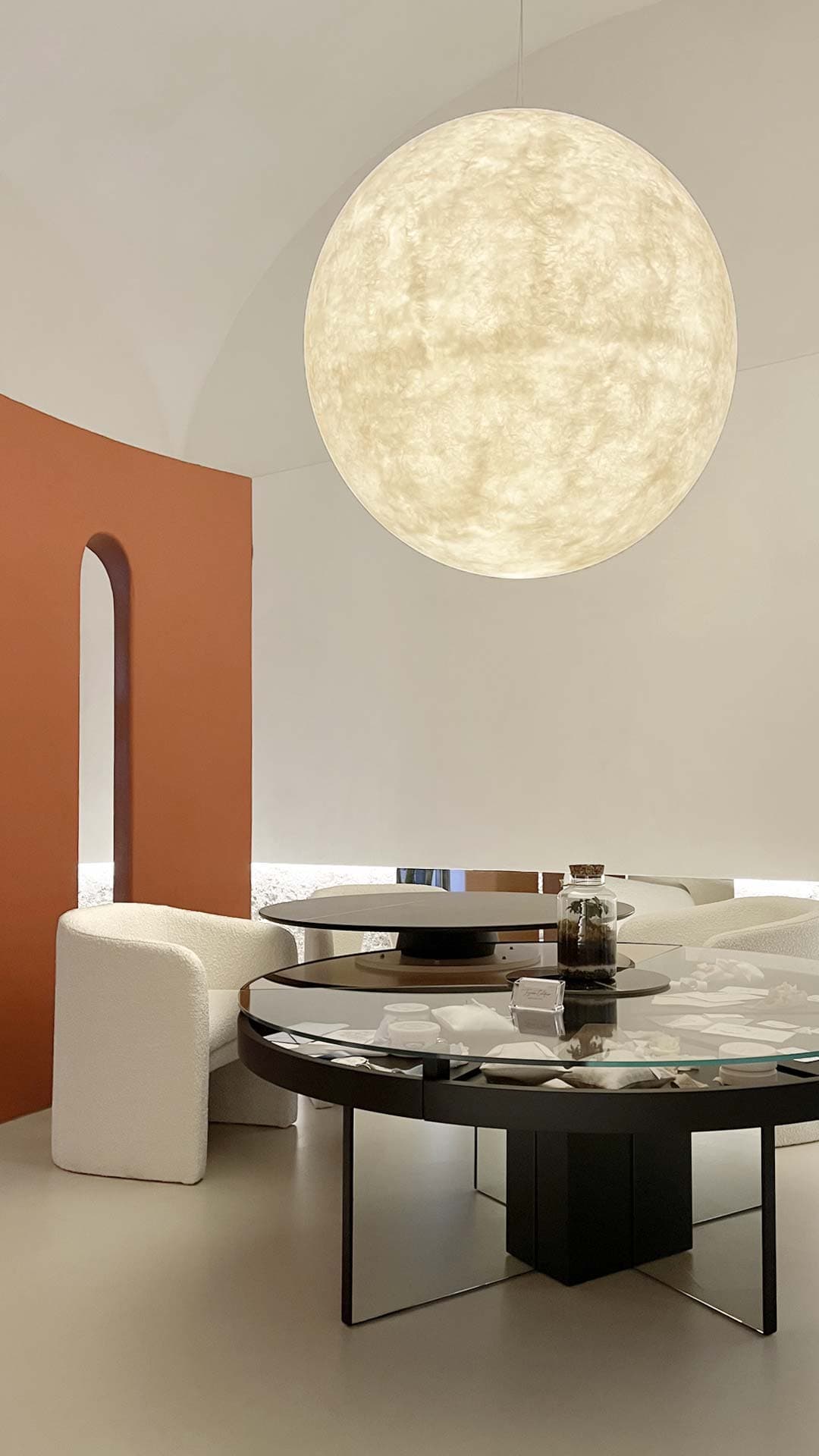 Modern room with a large spherical pendant light, round glass table, white chairs, and a curved terracotta accent wall with an archway.