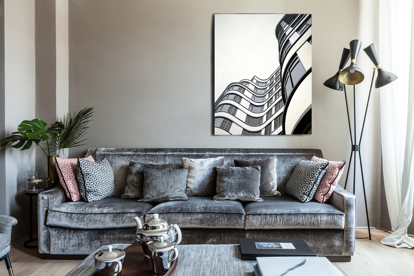 Modern living room with a gray sofa, assorted cushions, abstract wall art, a tall floor lamp, and a coffee table with a silver tea set.