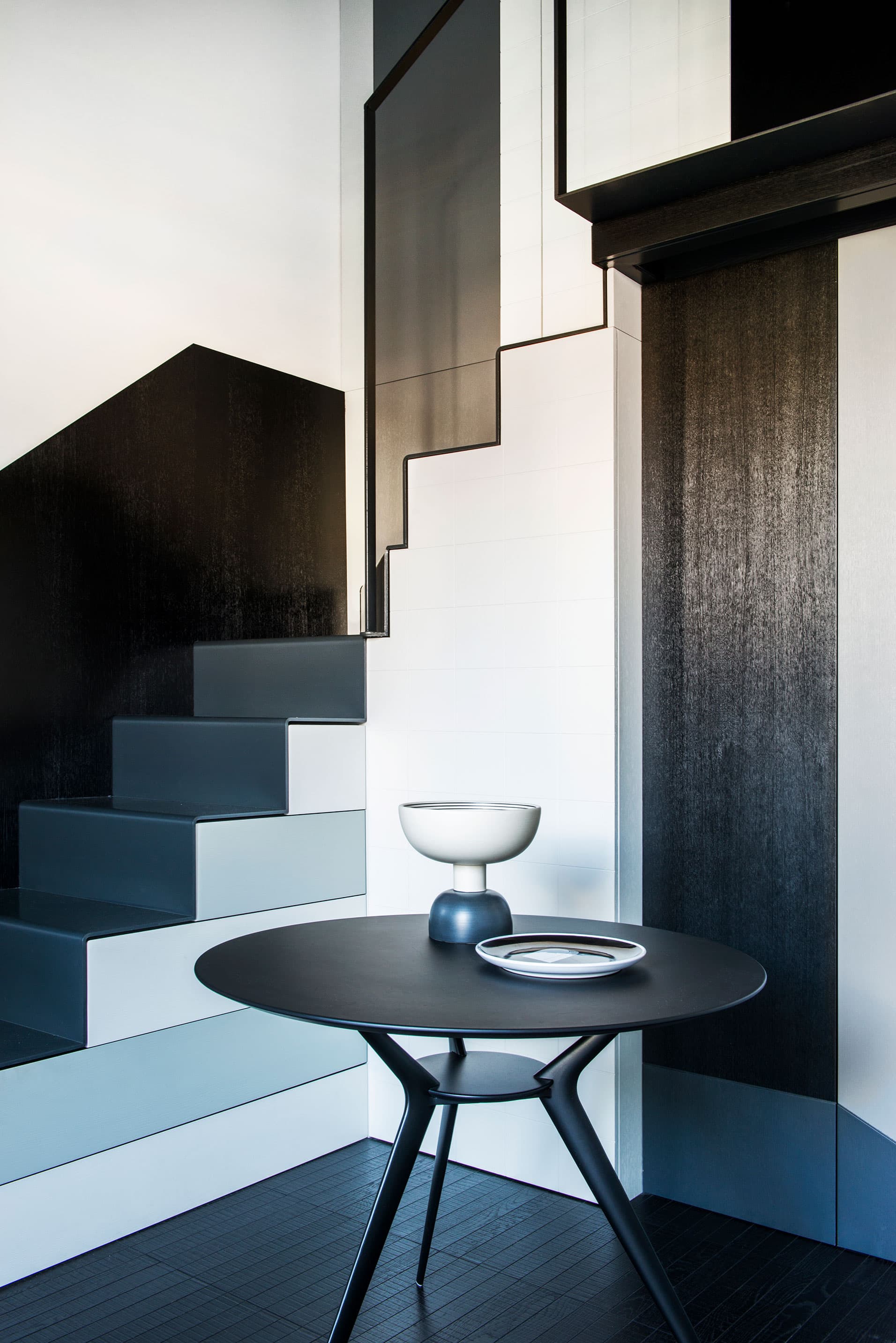 Modern interior with staircase, a sleek black round table, and a decorative plate on top.