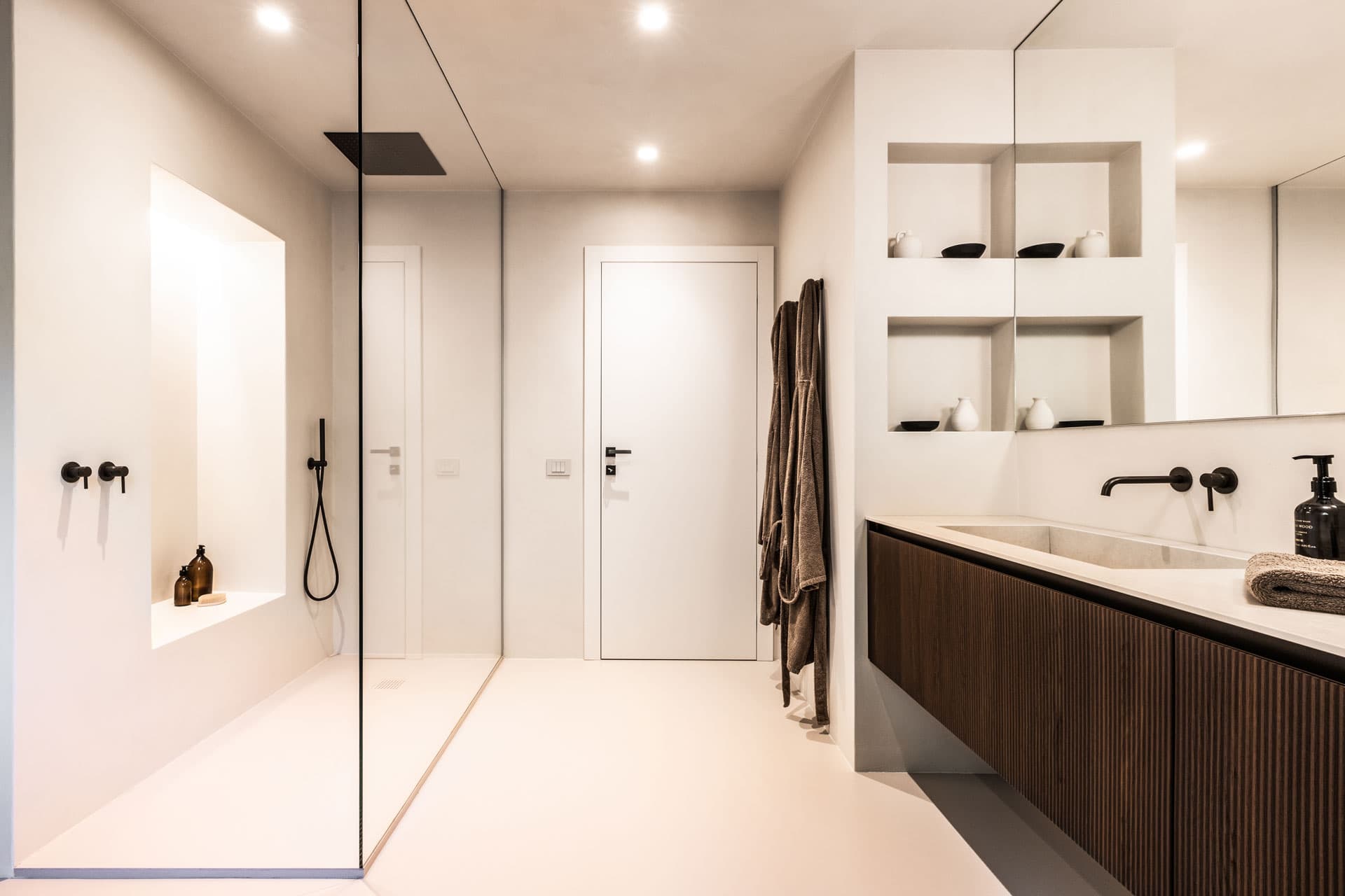 Modern bathroom with a glass shower, white walls, dark wood vanity, large mirror, and recessed shelves with decorative items.