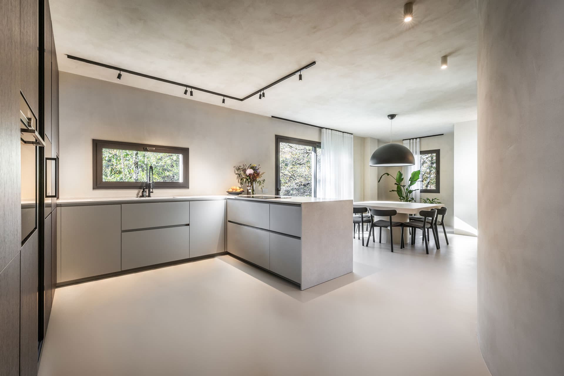 Modern kitchen with sleek grey cabinets, a central island, large windows, and a dining area with a table and black chairs.