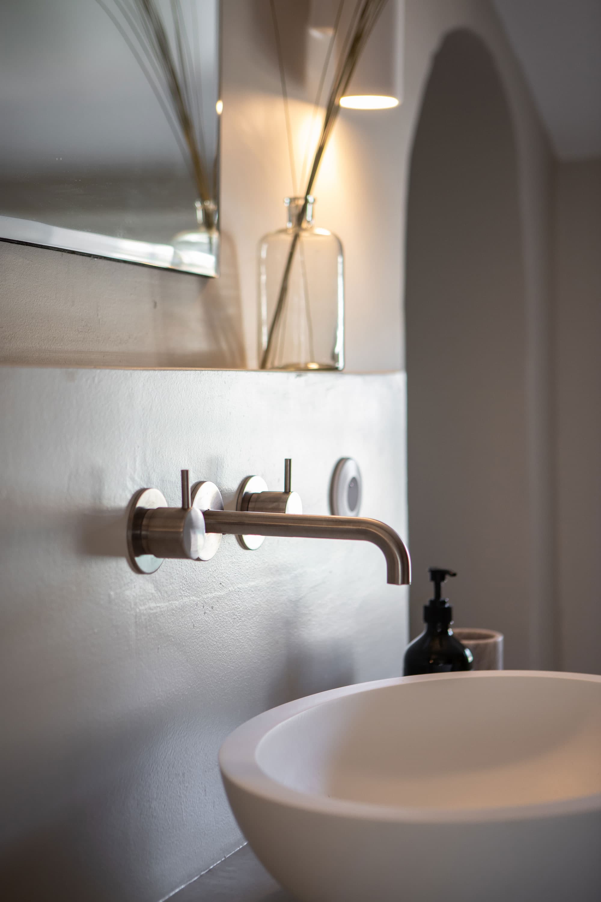 Minimalist bathroom with a round white sink, wall-mounted faucet. Soft lighting enhances the modern design.